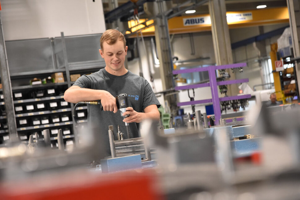 Junger lächelnder Werkzeugmacher in einer Produktionsumgebung beim Montieren eines Umformwerkzeugs in seinem Praktikum Job in Steyr bei weba.