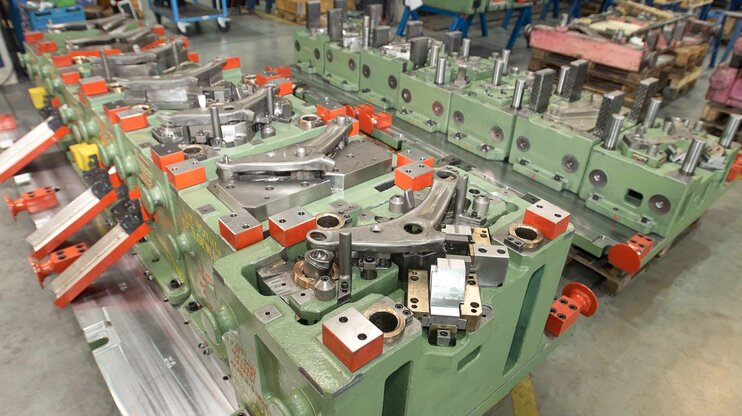 Transfer tool for a control arm in automotive production; complex tool setup with multiple forming stations and mechanical units in the weba Werkzeugbau facility.