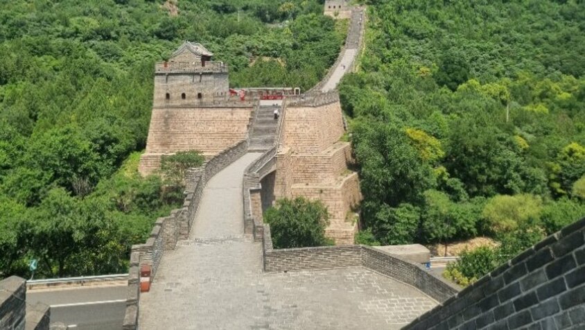 Blick entlang der Chinesischen Mauer, die sich über grüne Hügel und Täler erstreckt, mit Besuchern auf dem Weg – eine Station aus Jan Wengryns Zeit in China.