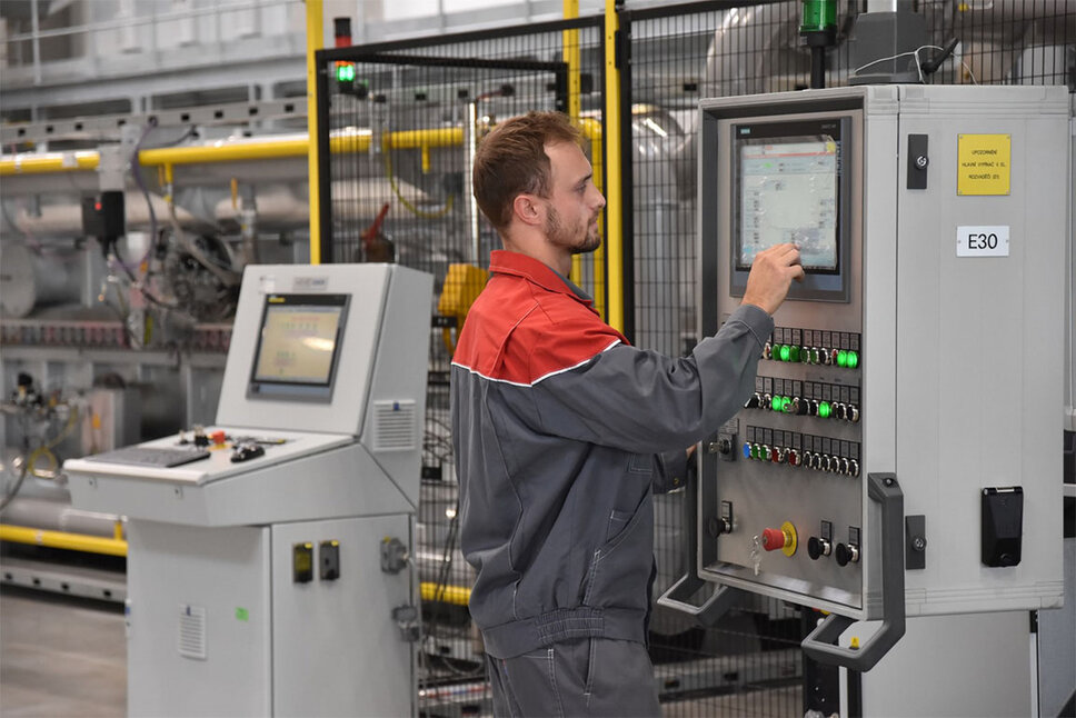 Ein konzentrierter Maschinenbediener der weba Werkzeugbau steht an der komplexen Steuerungskonsole der Warmformlinie, umgeben von leuchtenden Displays und Bedienelementen.