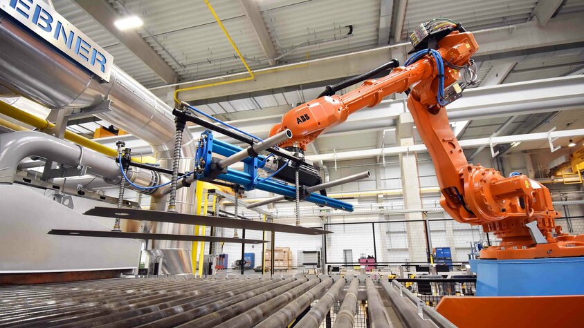 Industrieroboter hebt erhitzte Blechplatinen in einer modernen Warmumformungsanlage, um den Umformprozess vorzubereiten.