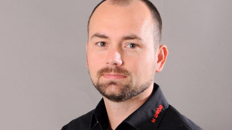 Portrét Radka Šimka, projektového manažera ve společnosti weba Werkzeugbau, v černé firemní košili před neutrálním pozadím.