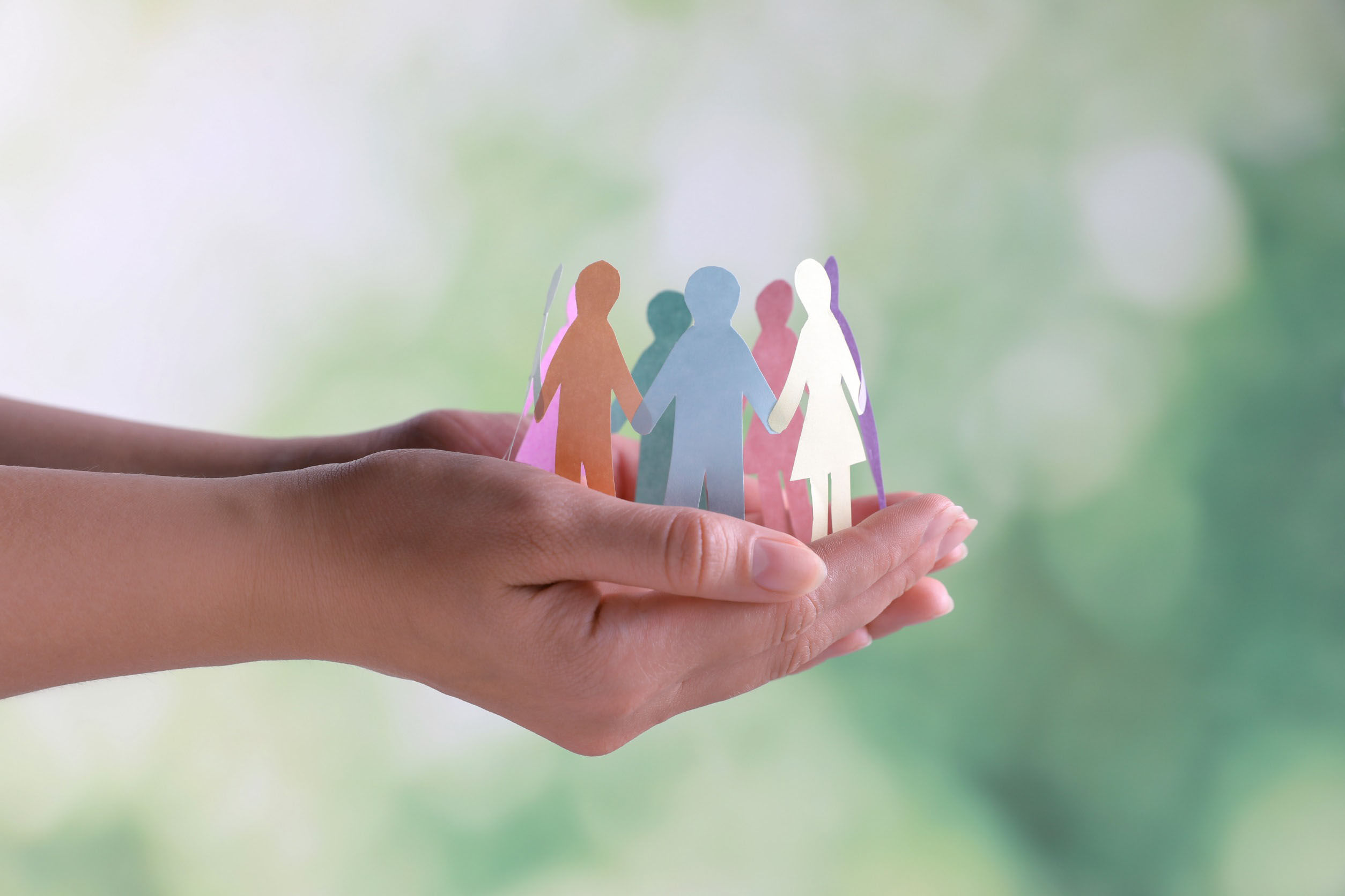 Close-up of hands holding paper cut-out human figures against a blurred background. This image illustrates the concept of diversity and inclusion. In the business ethics of weba Werkzeugbau, this image symbolizes the policy of respecting human rights and compliance with labor regulations.